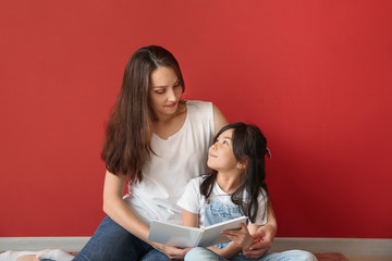 Mother with little daughter reading book near color wall