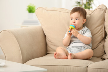 Cute little boy with nibbler sitting on sofa at home