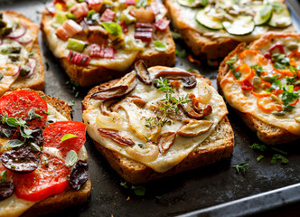 Vegetarian toast with grilled slices of bread with the addition of cheese and various vegetable toppings on a black background, close-up
