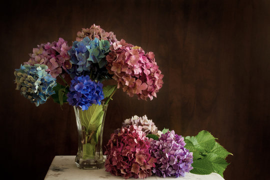Beautiful hydrangea flowers in multiple colors arranged in a vase on a table; Bright pink, purple and blue bunches of flowers