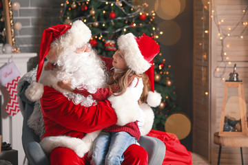 Santa Claus and little girl in room decorated for Christmas