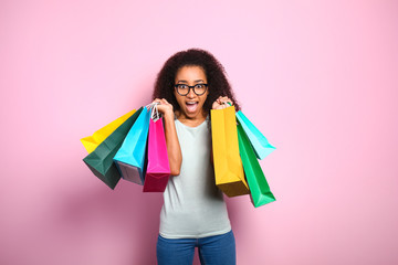 Portrait of excited African-American woman with shopping bags on color background