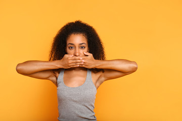Portrait of beautiful African-American woman covering mouth with hands on color background