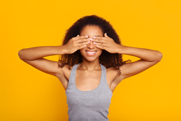 Portrait of beautiful African-American woman covering eyes with hands on color background