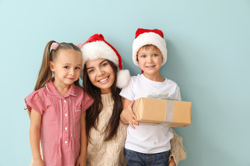 Woman and her little children with Christmas gift on color background