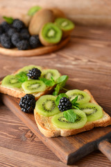 Tasty sandwiches with kiwi and blackberry on wooden board, closeup