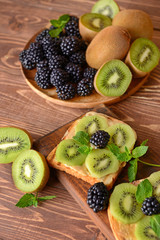 Tasty sandwiches with kiwi and blackberry on wooden table