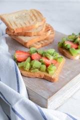 Tasty sandwiches with kiwi and strawberry on wooden board
