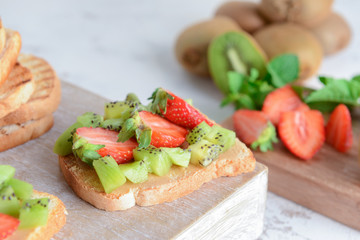 Tasty sandwich with kiwi and strawberry on wooden board, closeup