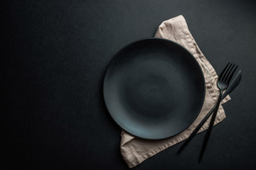 Black setting: plates, linen napkin and silverware on blfck background. Top view.