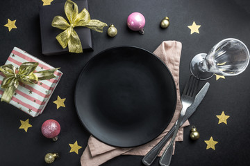 Christmas table setting with plate, silverware and decorations over black background