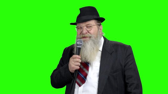 Senior showman with microphone on green screen. Elderly gentleman in suit and hat talking into microphone. Leisure activities concept.