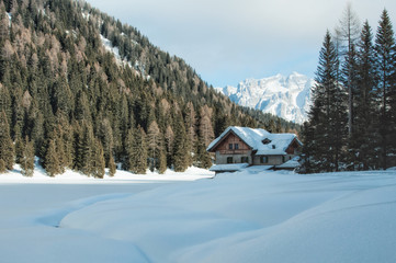 Wooden chalet by a snowy lake in winter in the Dolomites