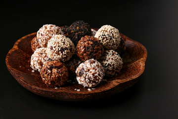 Energy balls of nuts, oatmeal and dried fruits on a wooden coconut plate on a dark background, horizontal orientation
