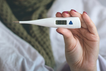 Flu sick woman is showing a thermometer with a high body temperature.