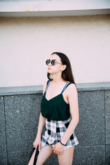 Sexy girl in a T-shirt, sunglasses and mini shorts near the wall