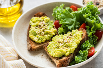 Breakfast avocado toast with seeds and green salad on plate, closeup view