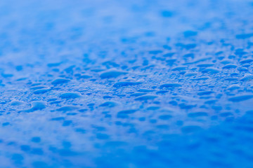 Several dew waterdrops on blue surface on a car