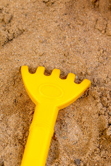 Yellow toy rake in the sandbox for children to play