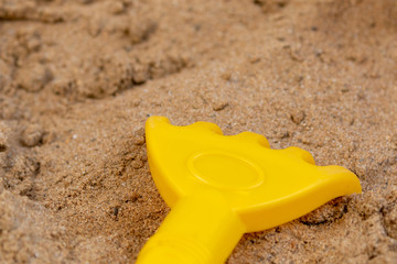 Close up of yellow plastic rake laying in the sandbox 