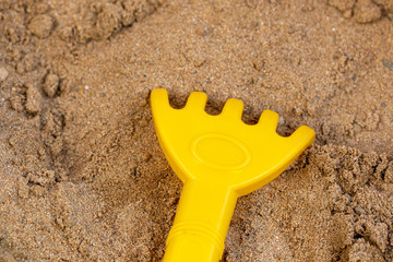 Small yellow rake lying in the sand in the sand box for playing