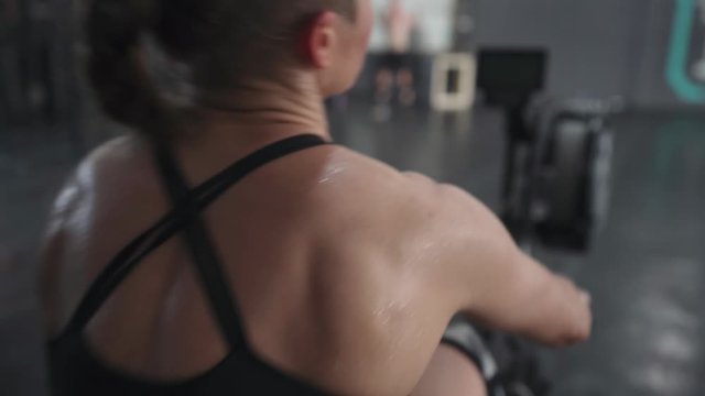 sporty girl does rowing exercise on the training apparatus in the gym. view from the back.