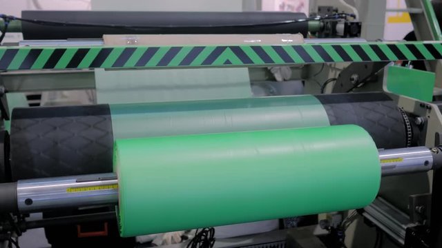 Part of automatic plastic bag making machine - moving roller with flat polyethylene green film at exhibition, trade show. Manufacturing, recycling, industry and automated technology equipment concept