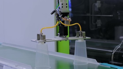 Automatic production line with robotic arm and moving polypropylene clear cups on conveyor belt of plastic injection molding machine at factory, exhibition. Manufacturing, industry, technology concept