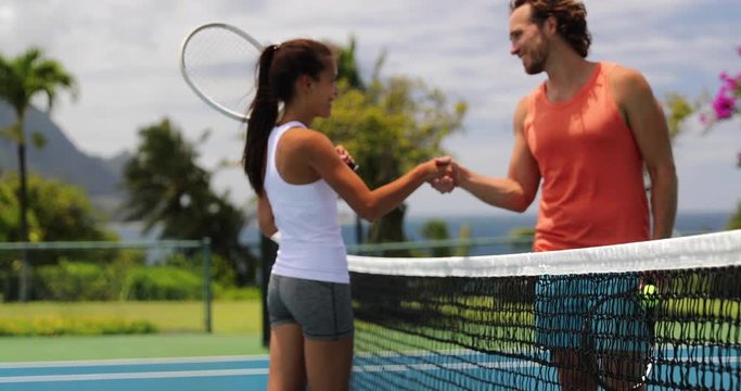 Tennis - tennis players shaking hands at net after match at beautiful outdoors tennis court. Woman and man holding tennis rackets giving handshake. focus on foreground. 59.94 FPS.