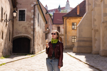 Fototapeta na wymiar Girl and ice cream. Walk through Bratislava. Leather jacket and sunglasses. Sun in her hair and a green scarf. On the old street.