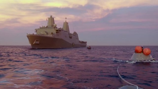 Aerial drone footage captures the recovery of a test re entry spacecraft at sea by a large military boat, sunset, 2019