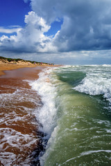 Scenic vertical landscape of sandy Black Sea beach by Anapa resort, Russia. Stormy waves splashing against beach sand on blue sky and clouds background on sunny summer day. Sea surf at storm.