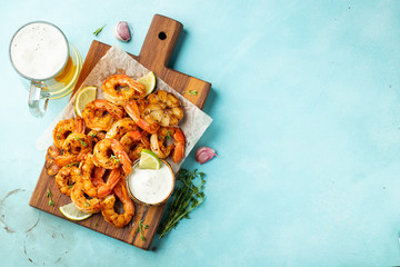 Grilled shrimp skewers or langoustines served with lime, garlic and sauce on a light blue concrete background. Seafood and beer. Top view with copy space. Flat lay
