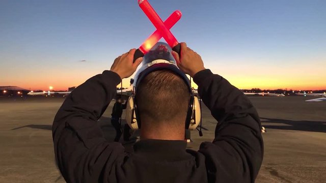 A man with orange batons stands in front of an idle F-16, 2019