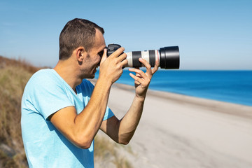 young male photographer with a large professional camera on the background of the sea and beach
