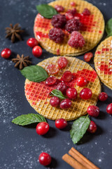 Sweet dessert on dark background. Traditional breakfast with gaufre, waffle, crispy wafer with red cherry berries, mint, fruits and syrup.