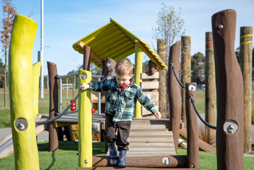 A little boy carefully practices walking across the swing bridge on the playground fort 