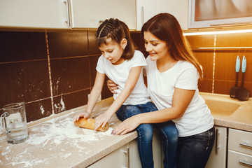 a young mother in a white t-shirt stands in the kitchen and works with flour along with her child