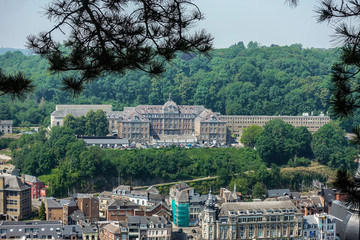 Dinant, Belgium - June 26, 2019: Seen from Citadelle. Large building is College Notre Dame de Bellevue, school system from primary to high school. Forests in back. Light blue sky.