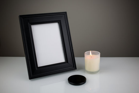 Empty blank black frame with place for text on a white table and burning candle with a black top on a side