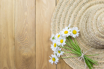 Straw hat, bouquet of daisies on a wooden background, top view. Copy Space. The concept of summer fashion. Vacation, weekend, summer.