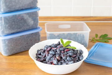 Ripe honeysuckle berries in containers on a wooden table. Harvesting berries for future use. Summer...