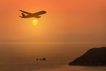 Naklejka na ściany i meble silhouette airplane flying above tropical sea in sunset 