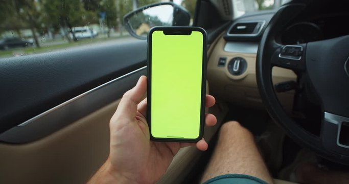 Close-up young man driver using mobile phone with green mockup chromakey technology in the car. Modern life concept.