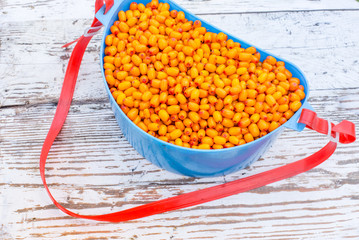 Sea buckthorn in a blue container on a wooden table. Autumn harvest of berries. Useful berry sea buckthorn.