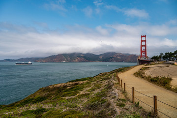 Fototapeta na wymiar Golden Gate bridge on the right with low clouds, ocean in the background and a gravel path heading towards the bridge