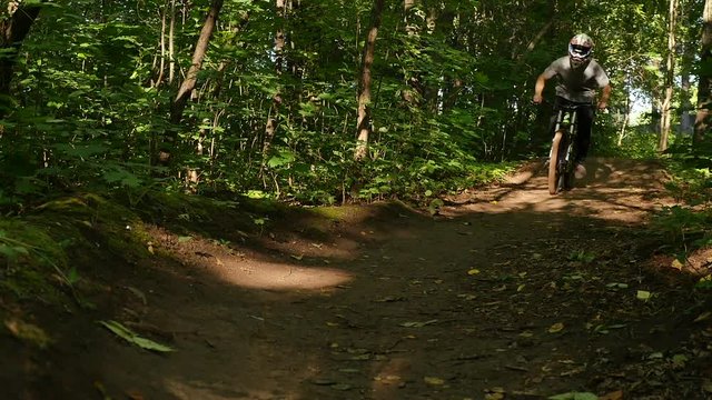 Young bicyclist in full face helmet riding on dh mtb on offroad in summer forest trail. Man cyclist riding on downhill full suspension moutain bike on dirty forest path. Active summer sport outdoor