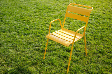 yellow metal chair stands on a lawn with green grass