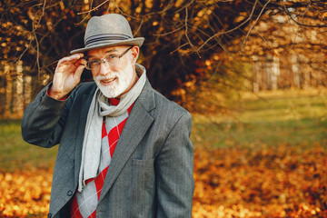 Handsome grandfather in a autumn park. Old man in a gray jacket and hat.