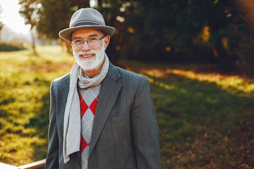 Handsome grandfather in a autumn park. Old man in a gray jacket and hat.